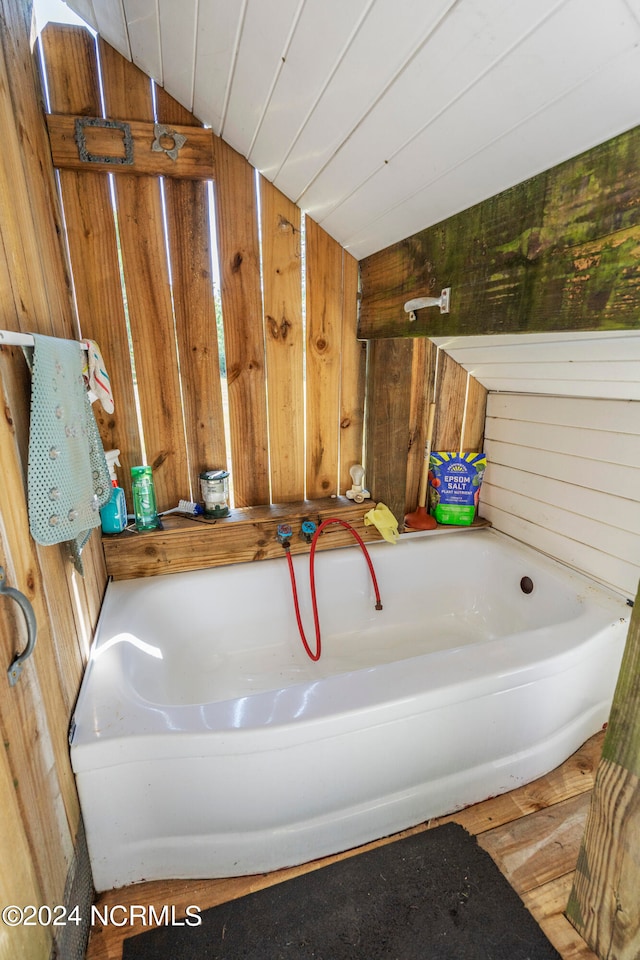 bathroom featuring wooden walls, a bathtub, and lofted ceiling