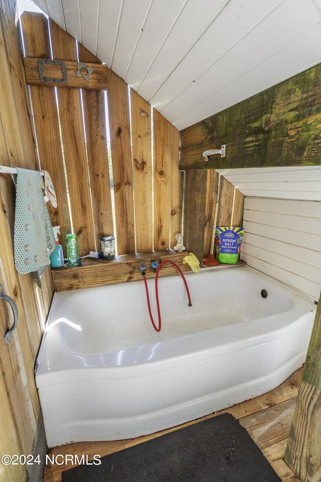 full bathroom with lofted ceiling, wood walls, a washtub, and wood finished floors