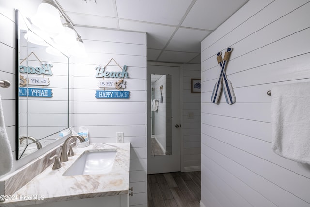 bathroom with wooden walls, a drop ceiling, vanity, and wood finished floors