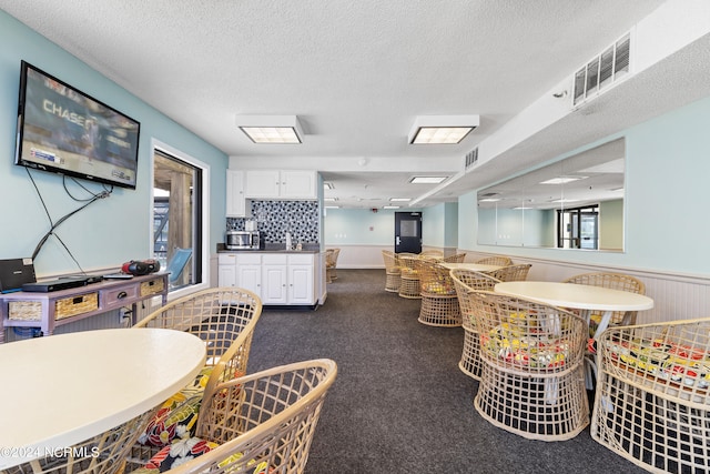 dining area featuring wainscoting, visible vents, a textured ceiling, and a bar