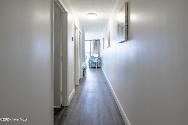 hall with a textured ceiling, baseboards, and wood finished floors