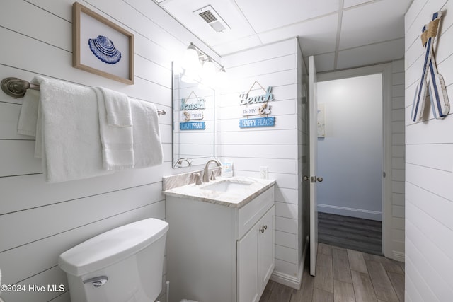 half bathroom with visible vents, wood walls, vanity, and toilet