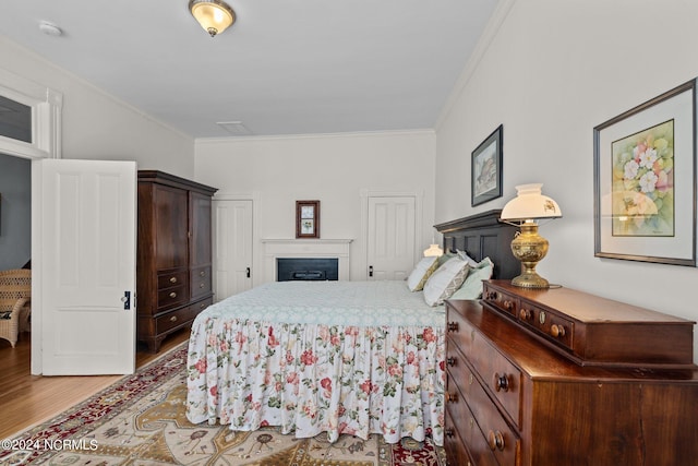 bedroom with ornamental molding, a fireplace, two closets, and wood finished floors