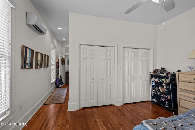 bedroom featuring a wall mounted air conditioner, baseboards, two closets, and wood finished floors