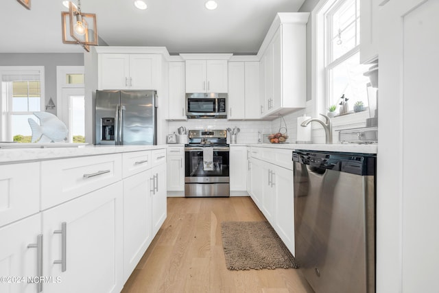 kitchen featuring light wood-type flooring, white cabinetry, stainless steel appliances, and backsplash