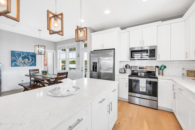 kitchen featuring white cabinets, stainless steel appliances, hanging light fixtures, and light hardwood / wood-style flooring