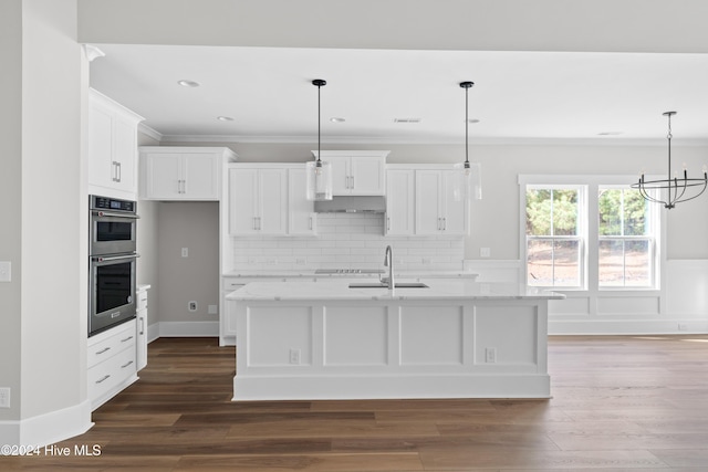 kitchen featuring light stone countertops, a center island with sink, white cabinets, and pendant lighting