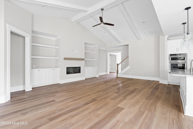 unfurnished living room with ceiling fan, built in features, beamed ceiling, high vaulted ceiling, and light hardwood / wood-style floors