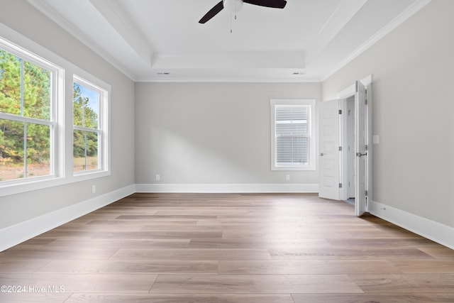 empty room featuring ceiling fan, crown molding, a tray ceiling, and light hardwood / wood-style flooring