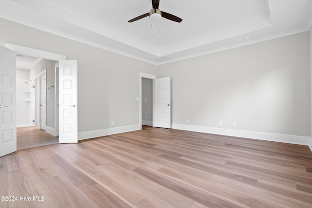 unfurnished bedroom featuring a tray ceiling, ceiling fan, crown molding, light hardwood / wood-style flooring, and connected bathroom