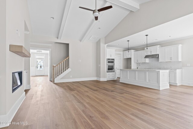 unfurnished living room featuring light wood-type flooring, ceiling fan, sink, beam ceiling, and high vaulted ceiling