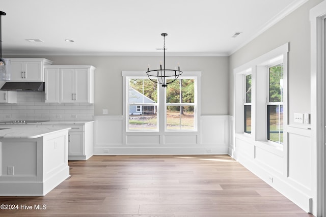 unfurnished dining area featuring light wood-type flooring, crown molding, a wealth of natural light, and an inviting chandelier