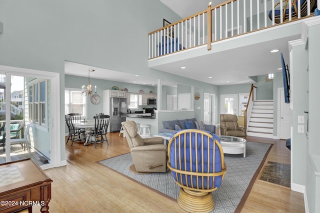 living area featuring light wood finished floors, baseboards, a towering ceiling, stairs, and a notable chandelier