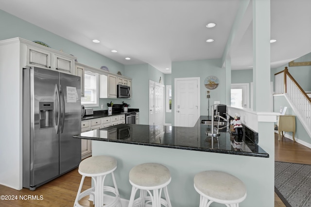 kitchen featuring a breakfast bar area, stainless steel appliances, recessed lighting, a sink, and wood finished floors