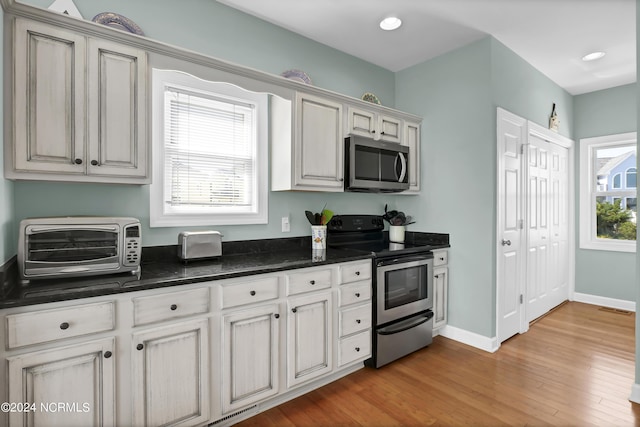 kitchen featuring baseboards, dark stone countertops, stainless steel appliances, light wood-style floors, and recessed lighting