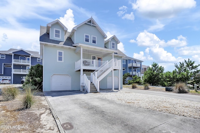 raised beach house with a garage, concrete driveway, a porch, and stairs