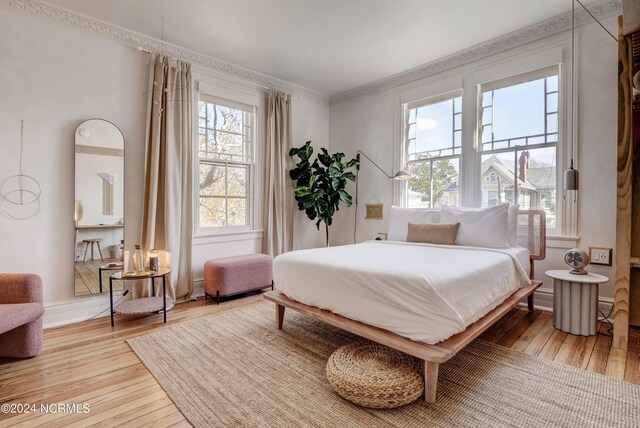 bedroom with ornamental molding, multiple windows, and light hardwood / wood-style floors