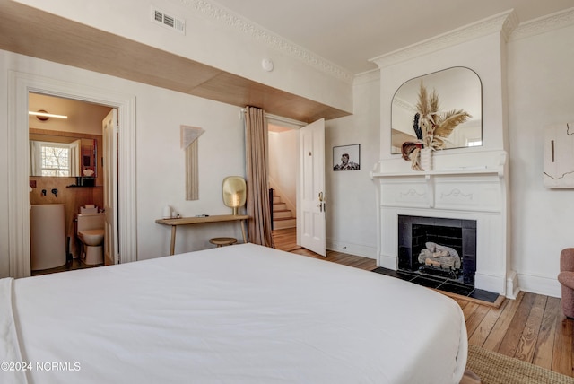 bedroom featuring ornamental molding, a tiled fireplace, hardwood / wood-style floors, and ensuite bathroom