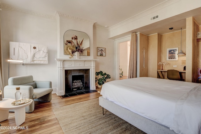 bedroom with crown molding, hardwood / wood-style floors, and a fireplace