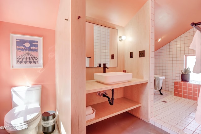 bathroom with toilet, tile patterned floors, sink, vaulted ceiling, and tile walls