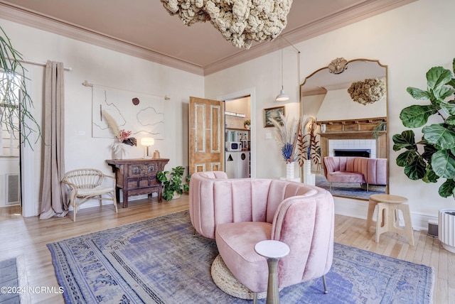 living room with wood-type flooring, a tile fireplace, a notable chandelier, and ornamental molding