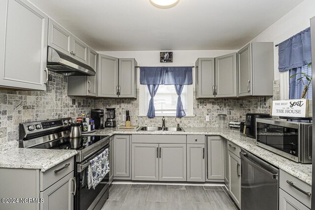 kitchen with appliances with stainless steel finishes, gray cabinets, a sink, and under cabinet range hood