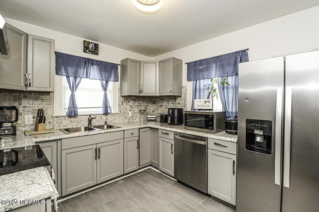 kitchen with tasteful backsplash, appliances with stainless steel finishes, a sink, and gray cabinetry