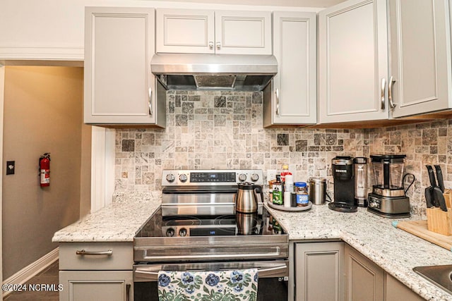 kitchen featuring light stone countertops, electric range, range hood, and tasteful backsplash