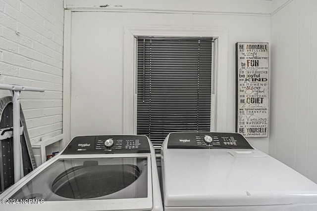 washroom with laundry area, washer and clothes dryer, and brick wall