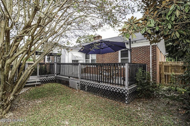 rear view of house featuring a deck, brick siding, a lawn, and fence