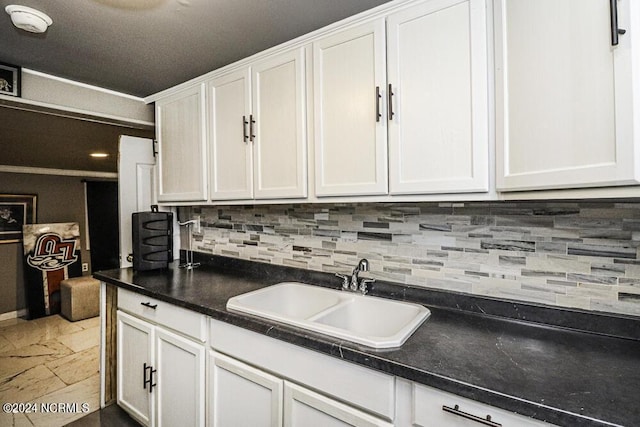 kitchen featuring decorative backsplash, dark countertops, a sink, and white cabinets