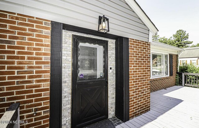 doorway to property featuring brick siding and a deck