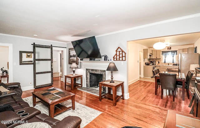 living room with crown molding, a barn door, a tile fireplace, and hardwood / wood-style flooring