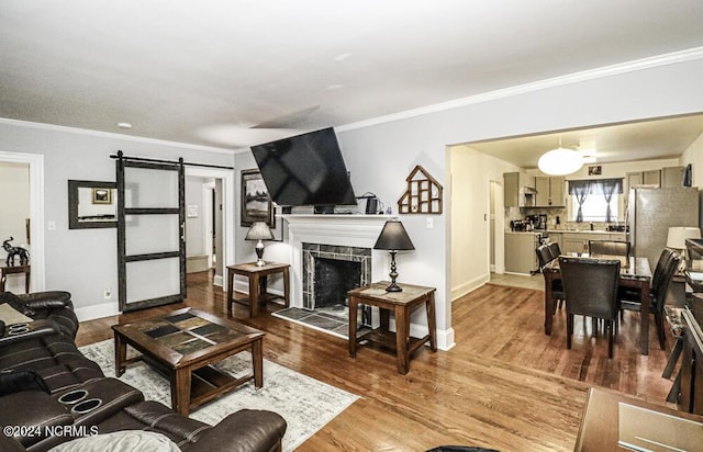 living area with ornamental molding, a barn door, a tiled fireplace, and wood finished floors