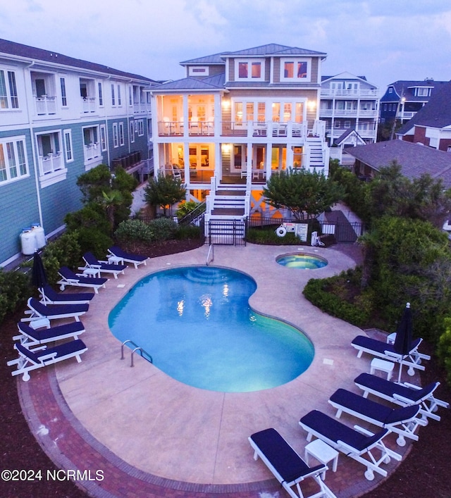 pool at dusk with a hot tub and a patio