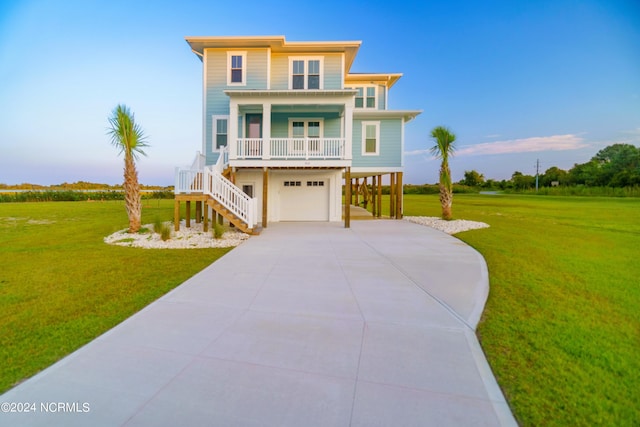 beach home with covered porch, an attached garage, a front yard, driveway, and stairs