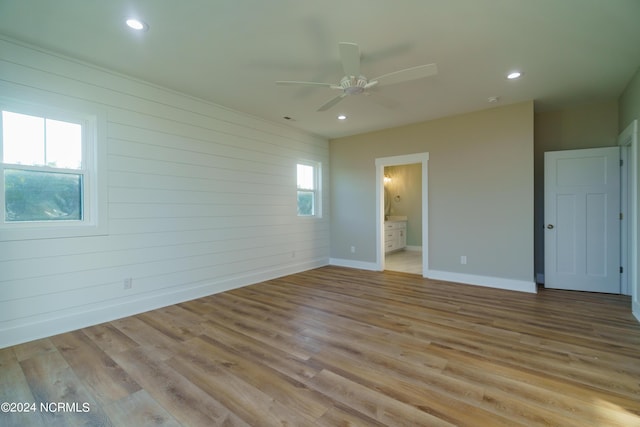 unfurnished room with a healthy amount of sunlight, ceiling fan, wood walls, and light hardwood / wood-style flooring