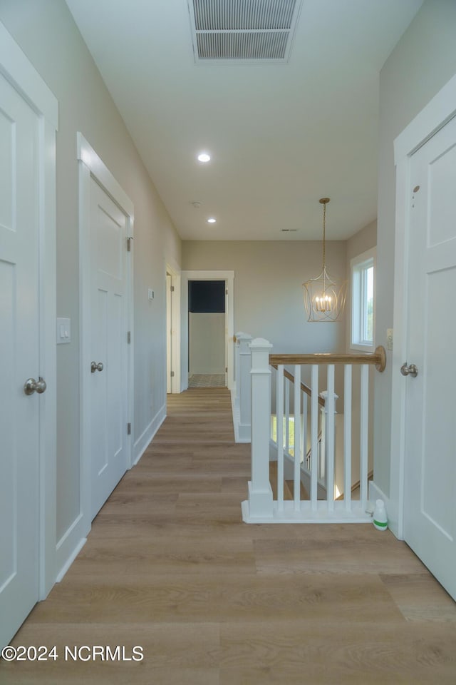 hall with light wood-type flooring and a chandelier