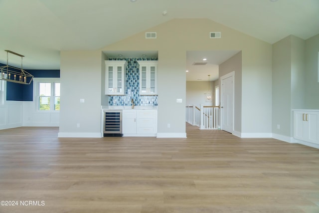 unfurnished living room featuring beverage cooler, lofted ceiling, and light wood-type flooring