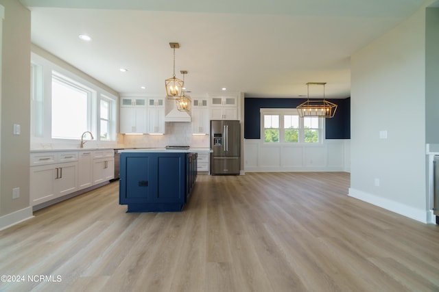 kitchen featuring light wood-type flooring, appliances with stainless steel finishes, white cabinetry, pendant lighting, and decorative backsplash