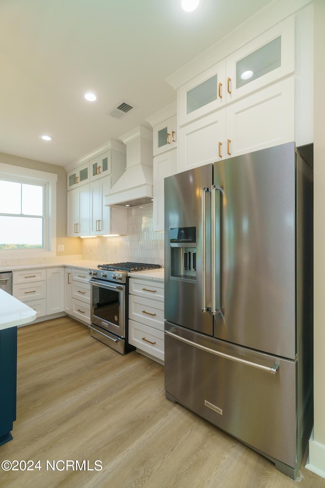 kitchen featuring light wood-type flooring, white cabinetry, stainless steel appliances, premium range hood, and decorative backsplash