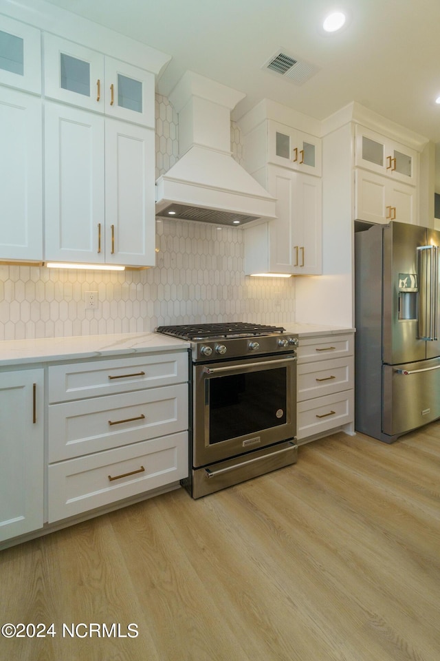 kitchen featuring light hardwood / wood-style flooring, custom range hood, stainless steel appliances, decorative backsplash, and white cabinetry