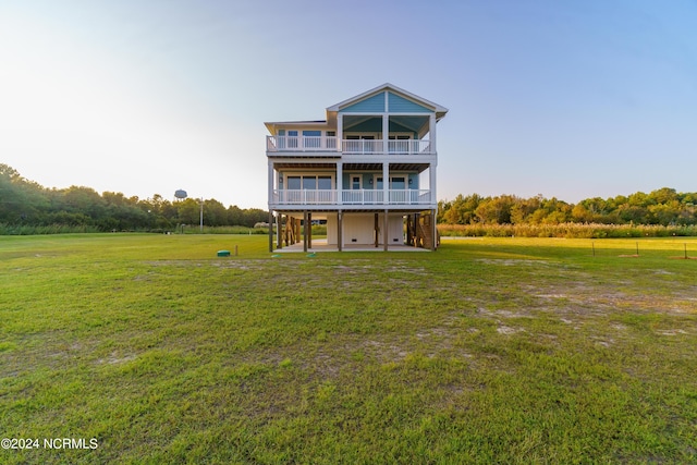 back of property with a lawn, a rural view, and a balcony