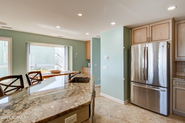 kitchen featuring light stone counters, sink, stainless steel refrigerator, decorative backsplash, and light tile patterned floors