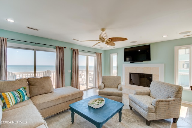 living room featuring ceiling fan, light tile patterned floors, a high end fireplace, and a water view