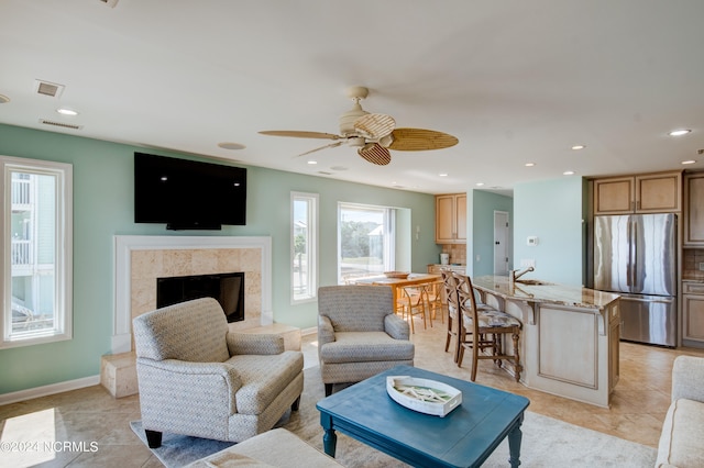 living room with a high end fireplace, ceiling fan, light tile patterned flooring, and sink