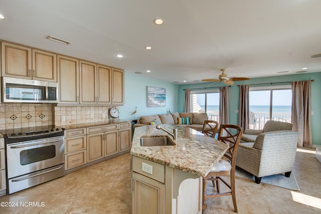 kitchen with an island with sink, stainless steel appliances, a water view, backsplash, and ceiling fan