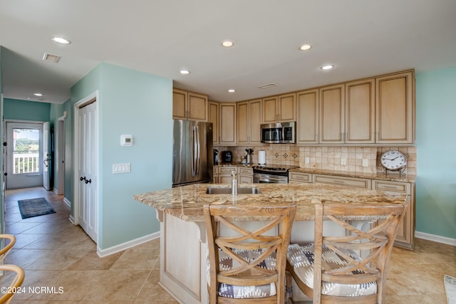 kitchen with a kitchen island with sink, appliances with stainless steel finishes, backsplash, and a kitchen breakfast bar