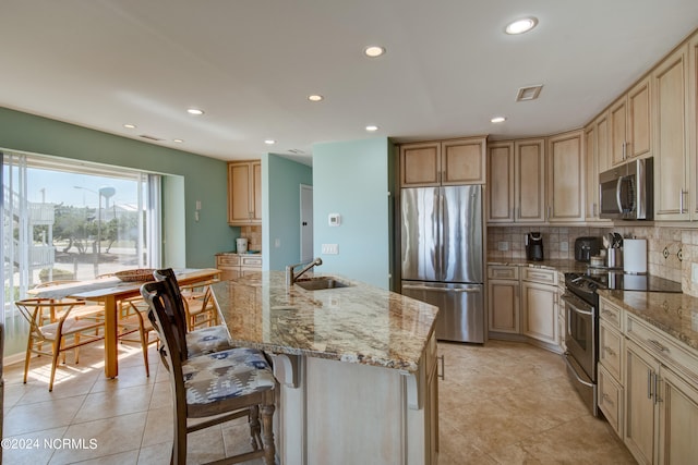 kitchen with light stone counters, a kitchen island with sink, stainless steel appliances, and sink