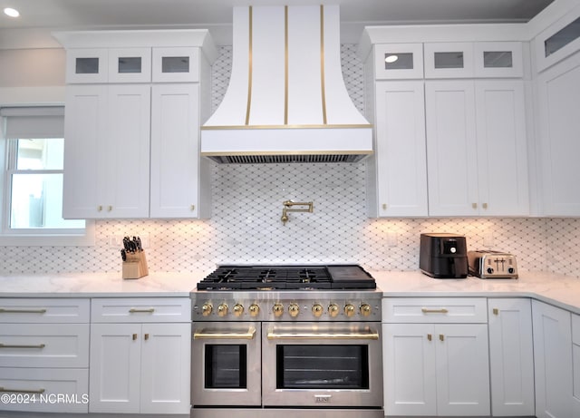 kitchen featuring range with two ovens, decorative backsplash, glass insert cabinets, white cabinetry, and premium range hood